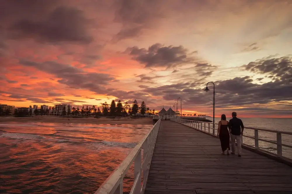 A couple walking along Glenelg jetty at sunset